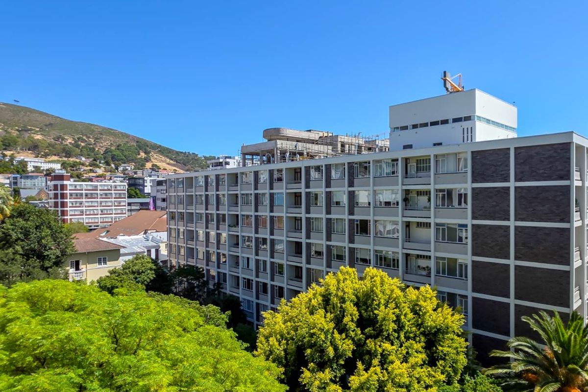 An elevated exterior view of a multi-story apartment building featuring a grid-like facade with balconies and large windows, set against a mountain backdrop.