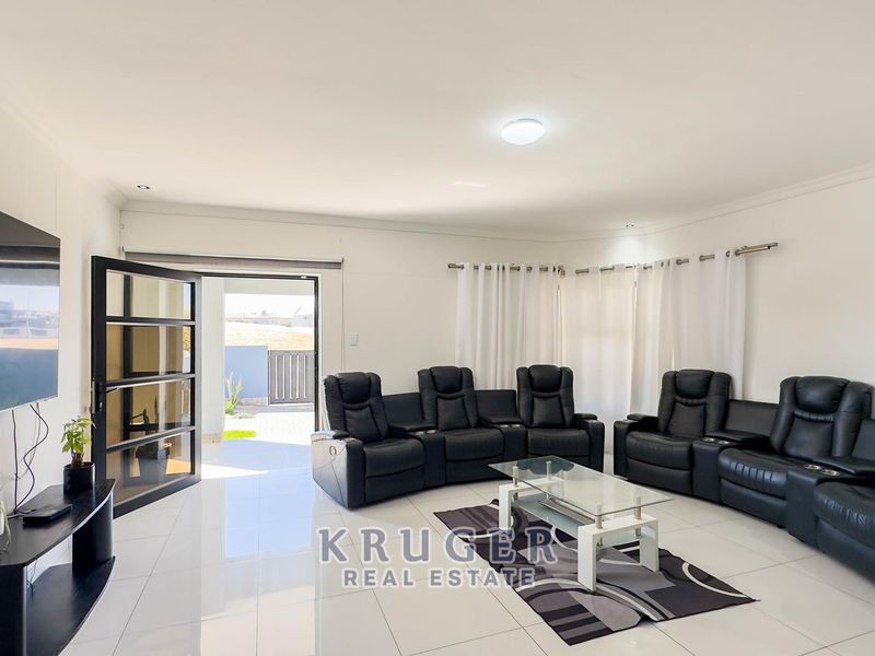 Spacious living room featuring polished white floor tiles, recessed lighting, and direct access to an outdoor patio area through a glass sliding door.