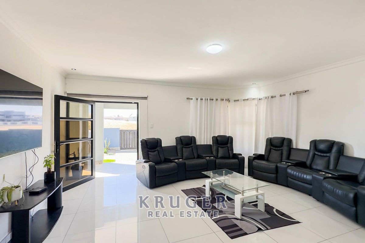 Spacious living room featuring polished white floor tiles, recessed lighting, and direct access to an outdoor patio area through a glass sliding door.