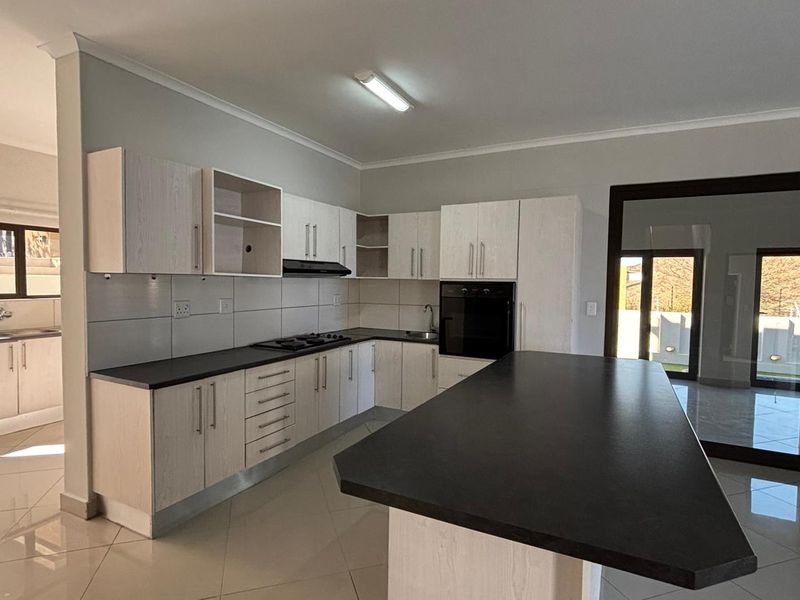 Modern kitchen featuring light wood-finish cabinetry, dark countertops, a central island, built-in oven and hob, and tiled flooring with access to an outdoor area.