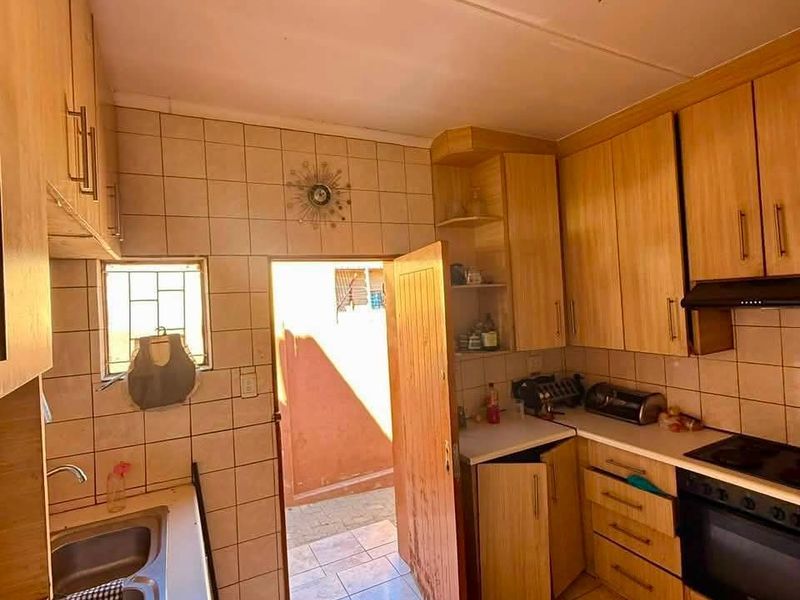 A dated kitchen featuring wooden cabinetry, a double basin sink, built-in oven and hob, with direct access to an outdoor area.