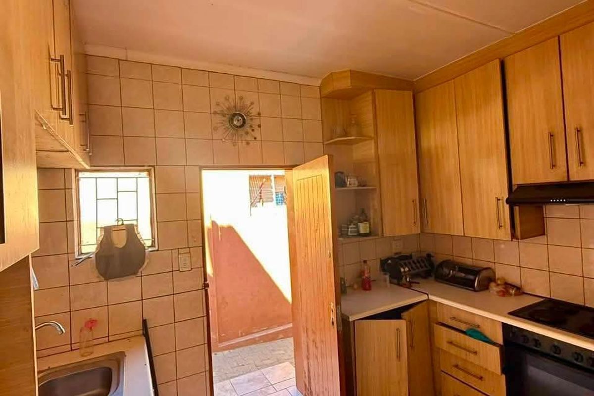 A dated kitchen featuring wooden cabinetry, a double basin sink, built-in oven and hob, with direct access to an outdoor area.