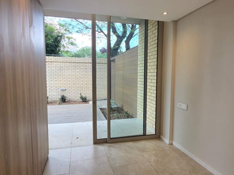 Modern living area featuring large sliding glass doors that open onto a private patio, complemented by sleek built-in cabinetry and neutral tiled flooring.