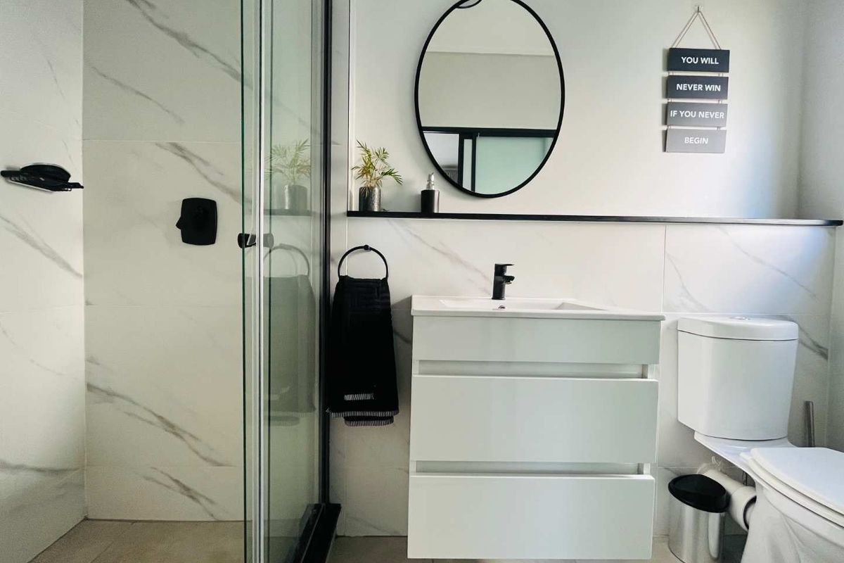 Modern bathroom featuring a walk-in shower with glass enclosure, wall-mounted vanity with basin, black fixtures, and elegant marble-look wall tiling.