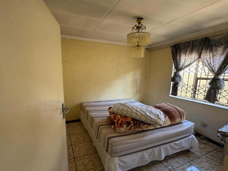 A bedroom featuring tiled flooring and security burglar bars on the window, requiring cosmetic updates to the wall finishes.
