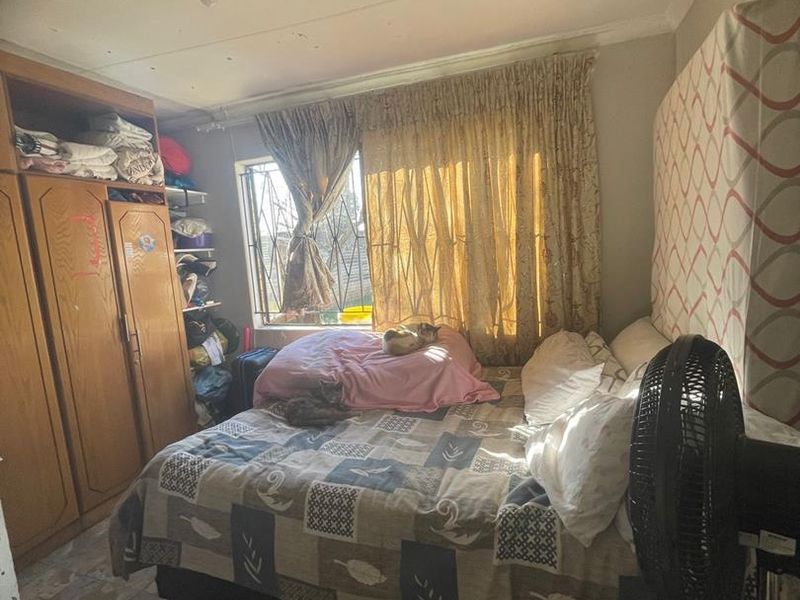 A bedroom featuring built-in wooden wardrobes, tiled flooring, and security bars on the window. The room requires cosmetic updates to improve its overall condition.