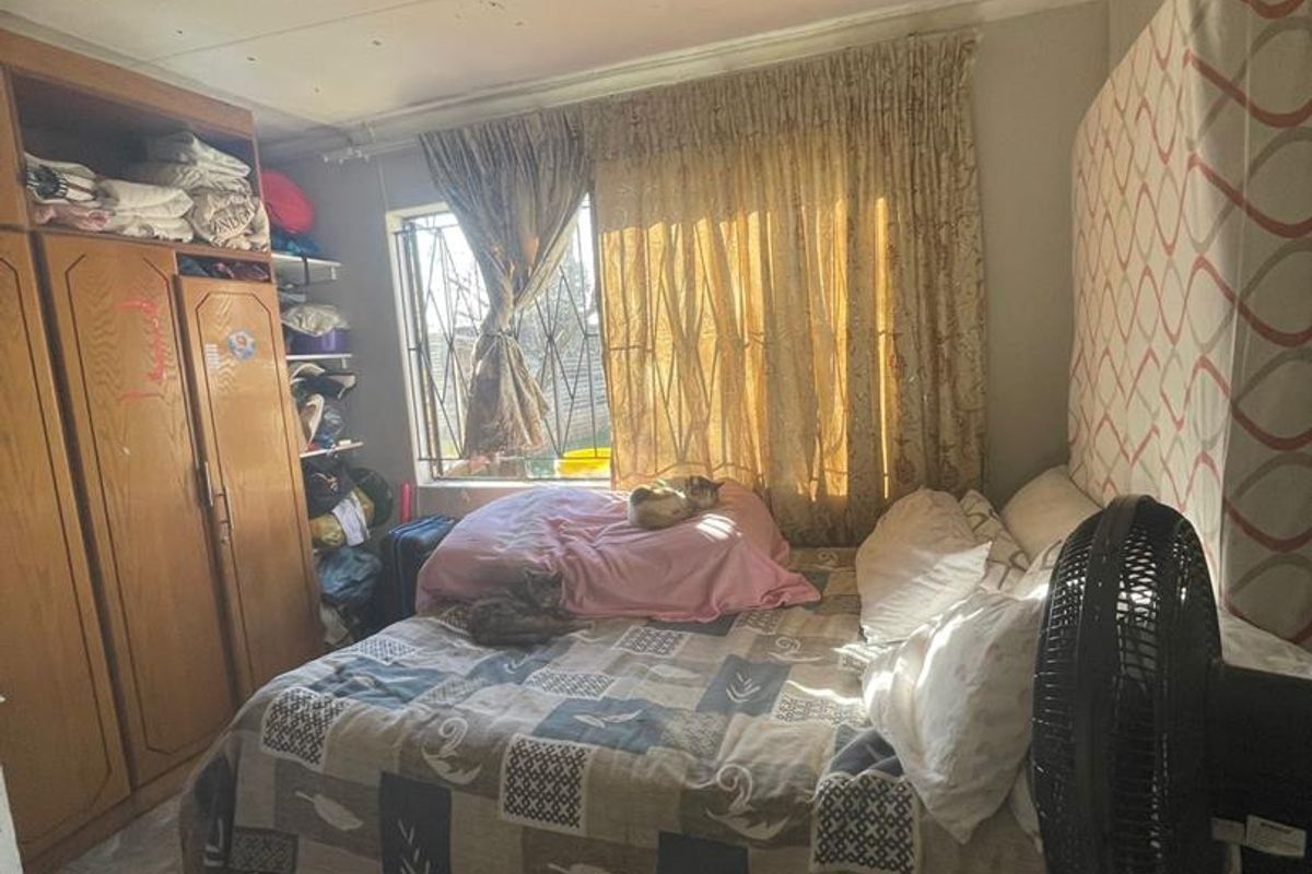A bedroom featuring built-in wooden wardrobes, tiled flooring, and security bars on the window. The room requires cosmetic updates to improve its overall condition.