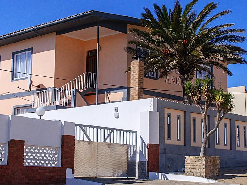 Front elevation of a two-story residential property featuring a brick boundary wall, metal gate, and an external staircase leading to an upper balcony.