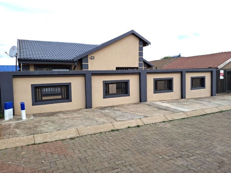 Front view of a residential property featuring a secure perimeter wall with security spikes, a tiled roof, and a paved driveway.