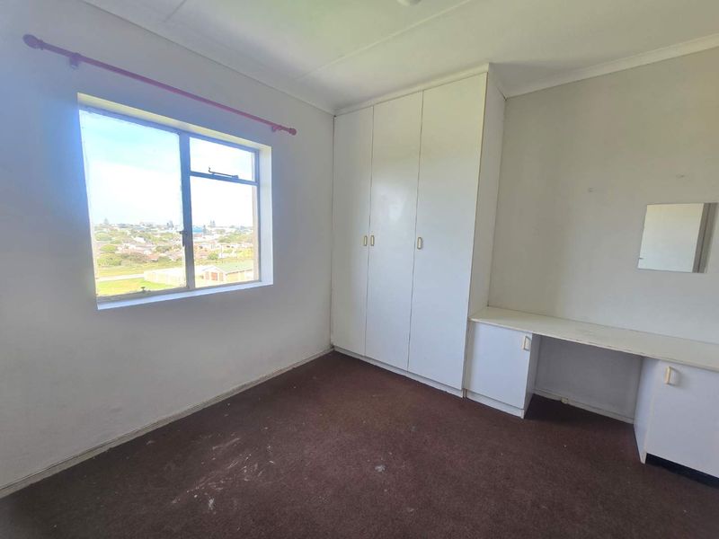 A vacant bedroom featuring built-in wardrobes, a built-in desk, and a window with an elevated view.