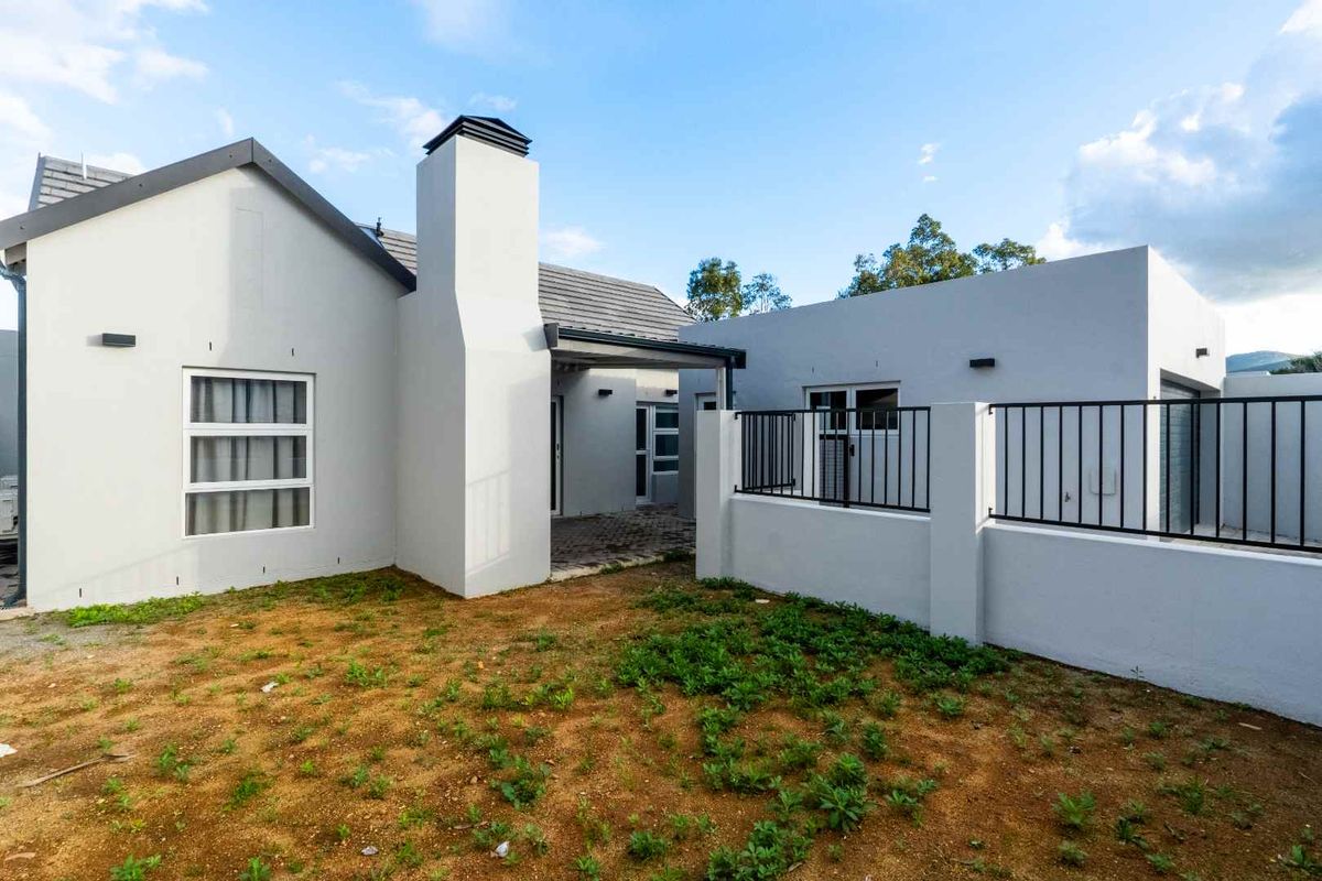 Rear view of the property featuring a paved patio area, a prominent chimney, and a fenced boundary wall with an unfinished garden space.