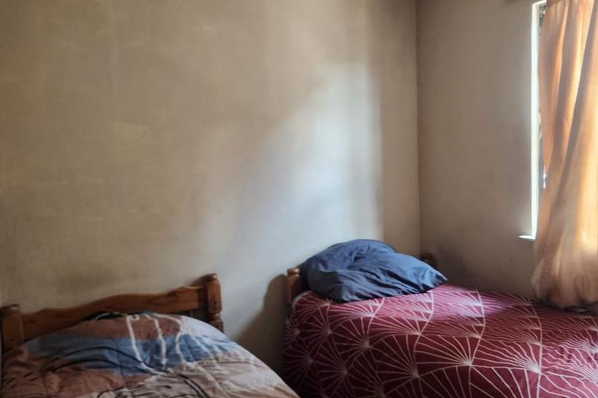 A bedroom featuring plain walls and a single window, currently furnished with two beds. The room requires cosmetic updates to improve its overall condition.