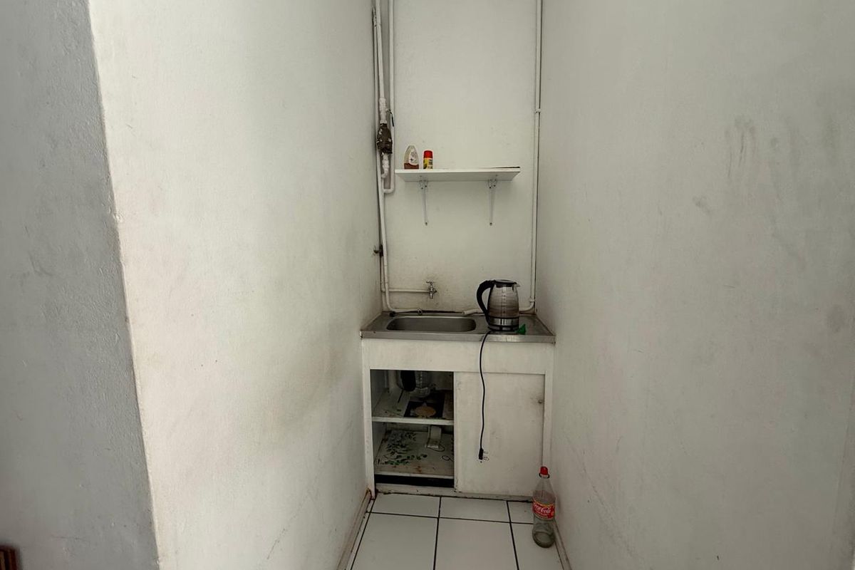 A compact kitchenette area featuring a stainless steel sink, base cabinetry, and wall-mounted shelving, requiring cosmetic updates and finish improvements.