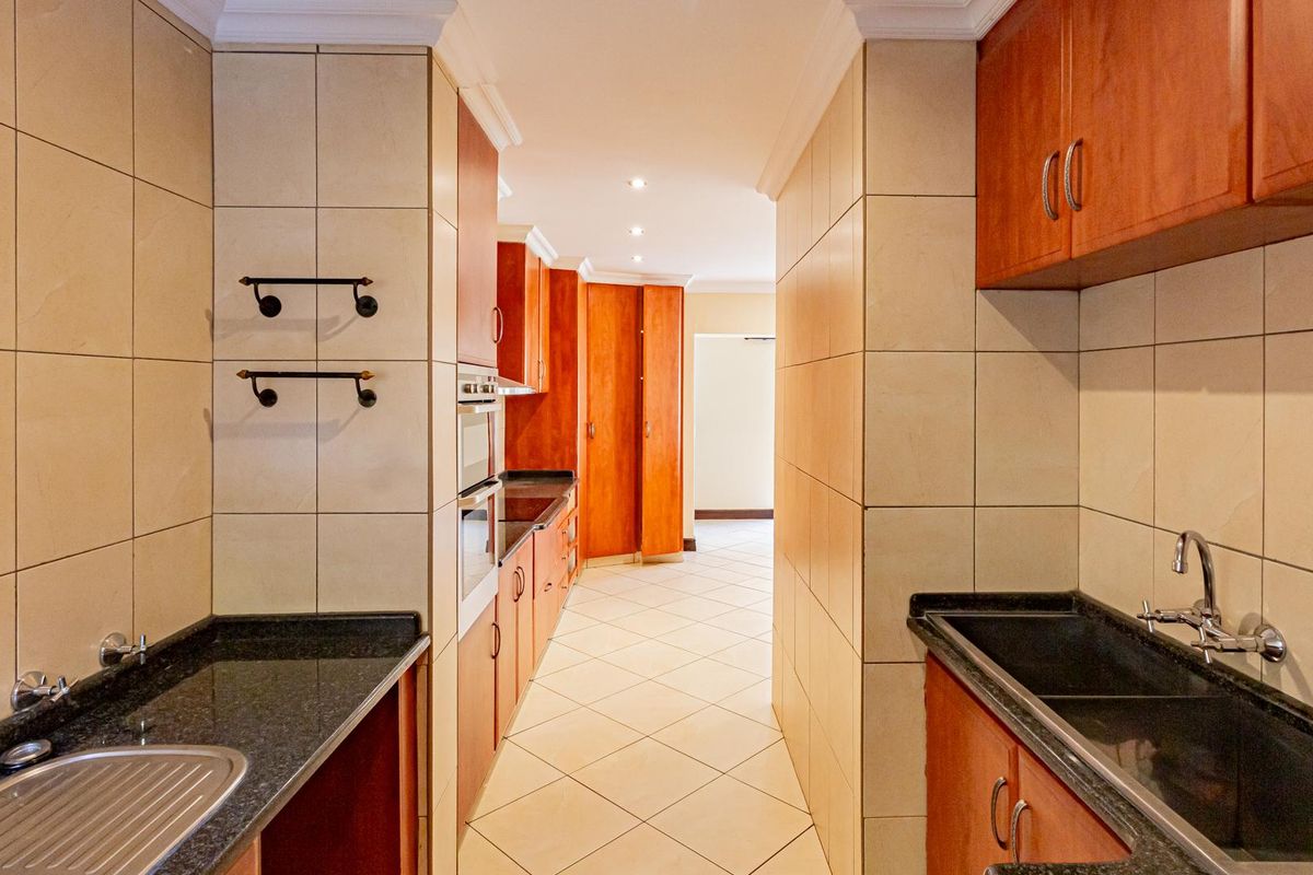 A functional galley-style kitchen featuring dark granite countertops, wooden cabinetry, tiled walls, and dual stainless steel sinks.