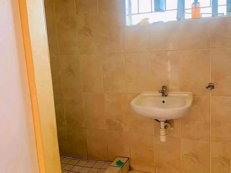 A functional bathroom featuring tiled walls and flooring, a wall-mounted basin, and a shower area, currently requiring some maintenance and cosmetic updates.