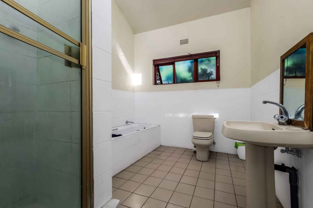 A dated bathroom featuring a pedestal basin, a built-in bathtub, a separate shower enclosure, and neutral wall tiles.
