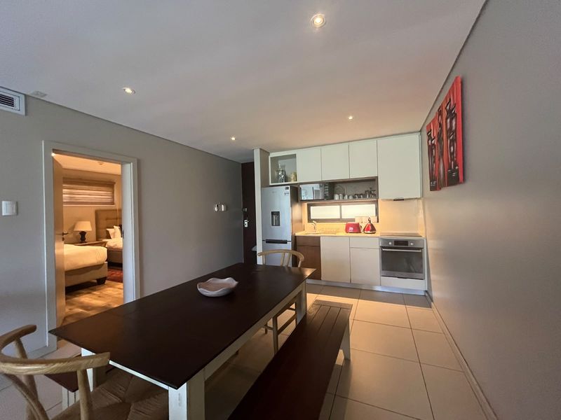 Open-plan living and kitchen area featuring modern cabinetry, built-in appliances, recessed lighting, and tiled flooring, with direct access to an adjacent bedroom.