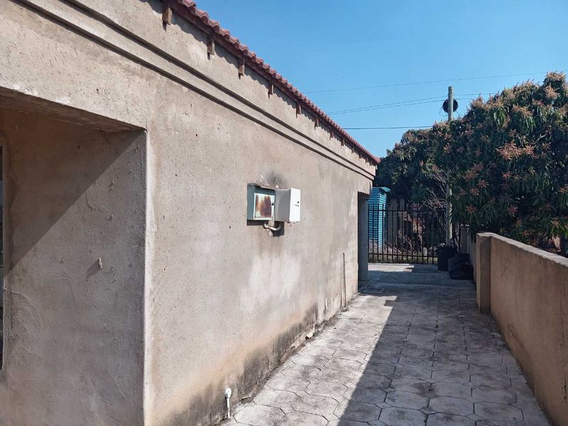 A side view of the property showing a paved walkway, boundary wall, and exterior wall with an electrical distribution box.