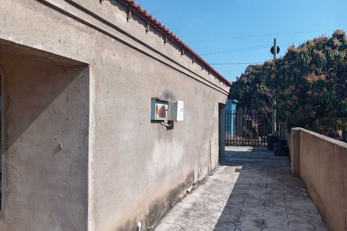 A side view of the property showing a paved walkway, boundary wall, and exterior wall with an electrical distribution box.