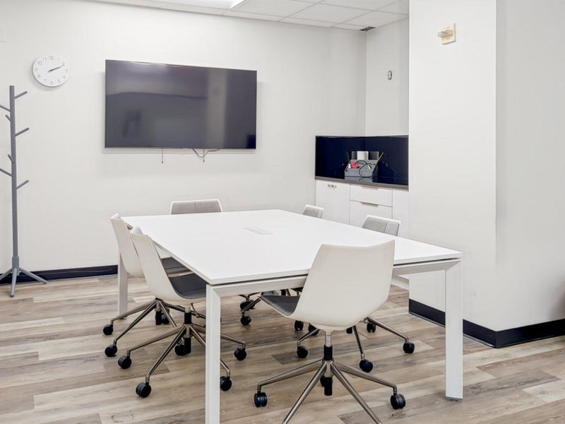 A modern office meeting room featuring laminate flooring, built-in cabinetry, and a suspended ceiling, providing a clean and professional workspace environment.