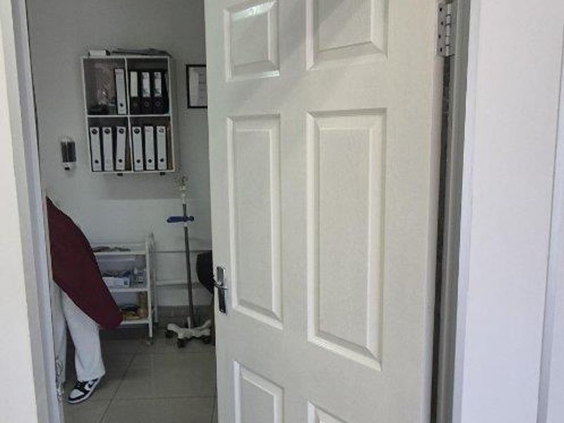 A view into a professional office space featuring a panelled door with signage, tiled flooring, and a suspended ceiling grid.