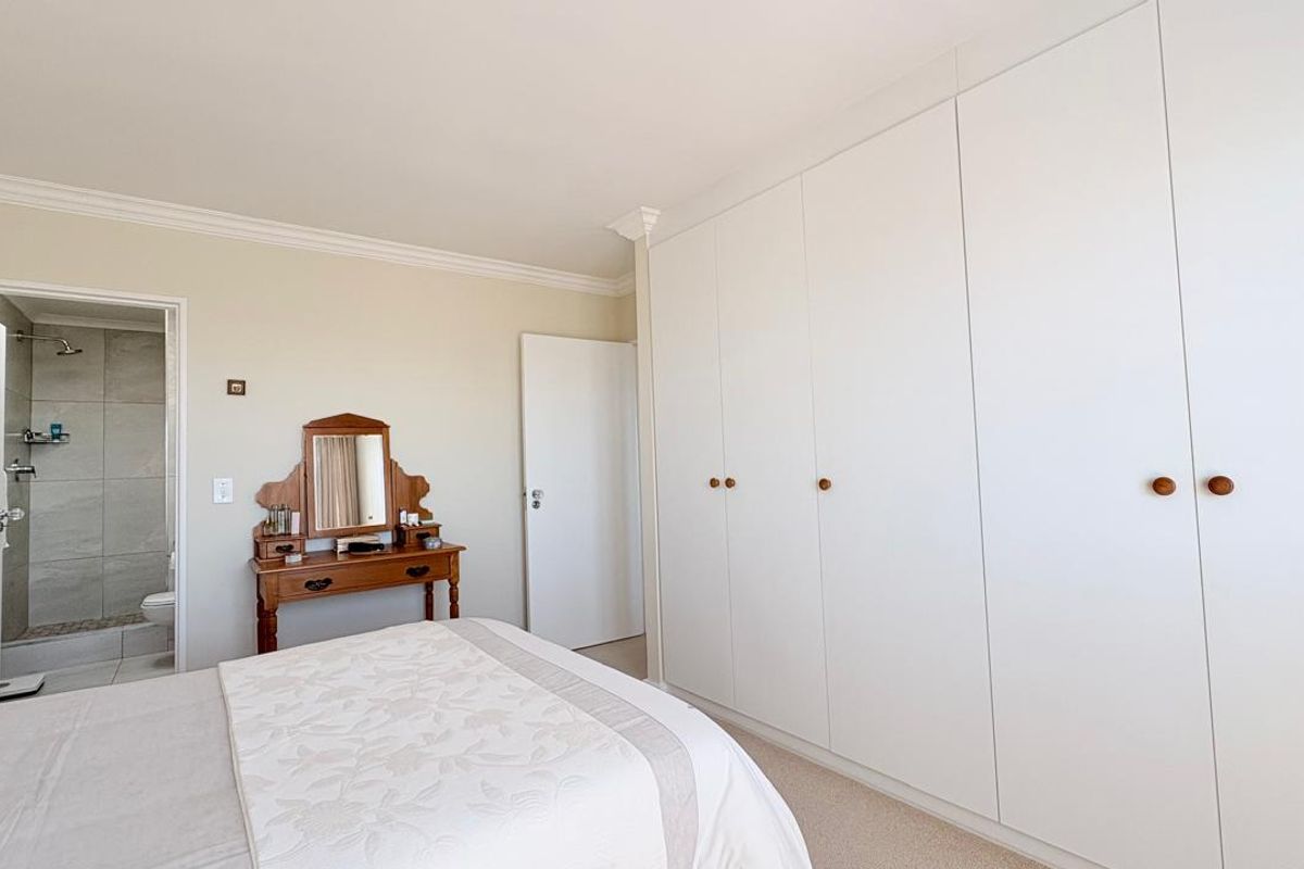 A bright bedroom featuring extensive built-in floor-to-ceiling wardrobes, crown molding, and an en-suite bathroom with a walk-in shower.