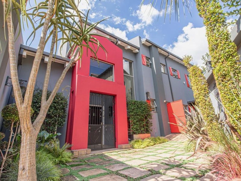 Modern front facade featuring a bold red entrance structure, grey exterior walls, and a paved driveway with integrated landscaping.