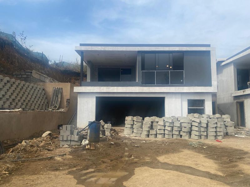 Rear view of a modern two-story house under construction, featuring a balcony with glass balustrade and a ground-level garage.