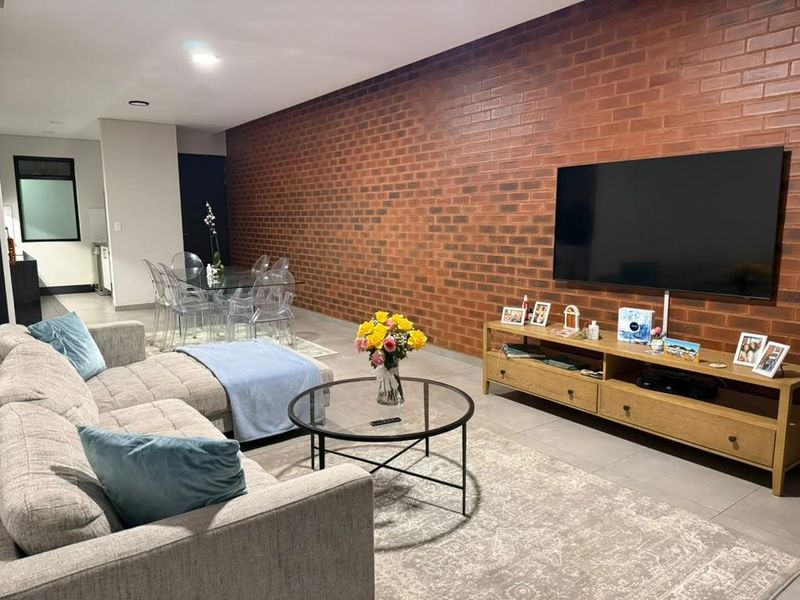 Spacious open-plan living and dining area featuring a prominent exposed brick feature wall, modern tiled flooring, and recessed downlighting.