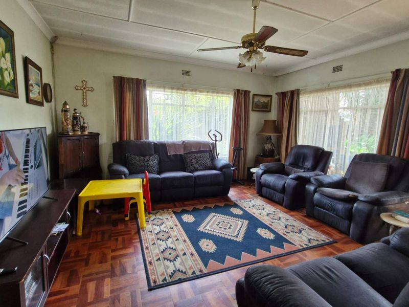 A spacious living room featuring classic parquet flooring, a ceiling fan, and large windows that provide ample natural light.