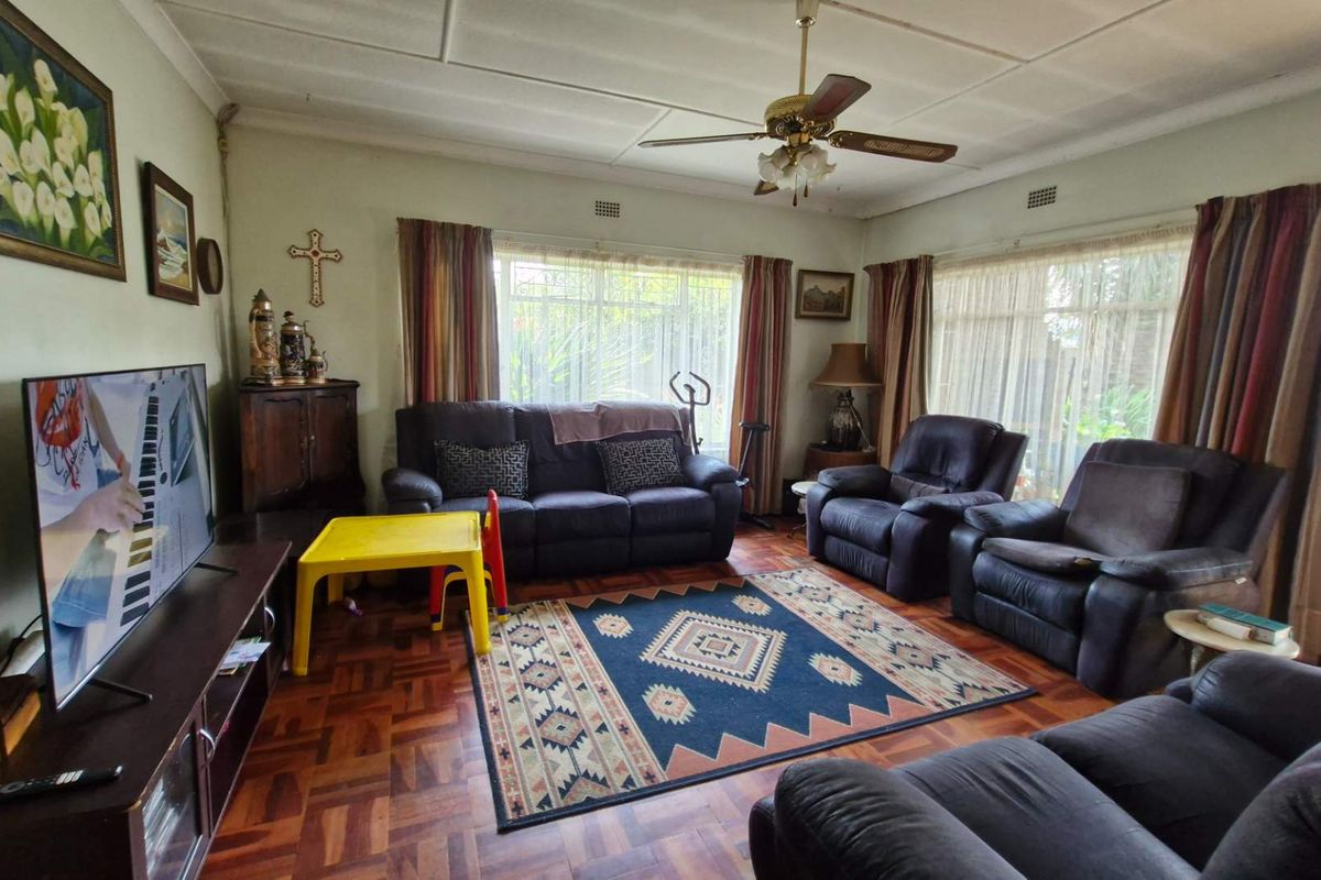 A spacious living room featuring classic parquet flooring, a ceiling fan, and large windows that provide ample natural light.