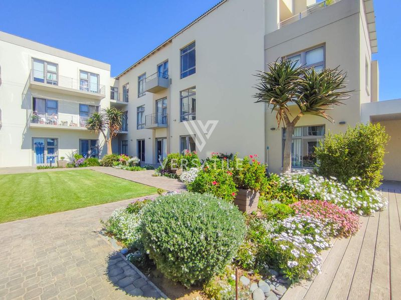 A well-maintained courtyard area within a retirement village, featuring landscaped gardens, paved walkways, and modern multi-story residential building facades with balconies.