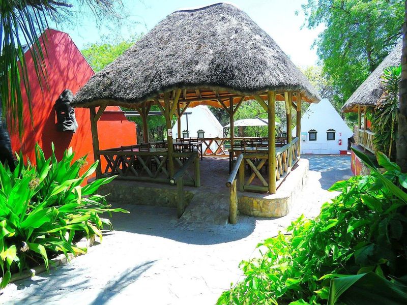 A charming outdoor thatched gazebo area featuring timber construction and stone detailing, set within a landscaped lodge garden environment.