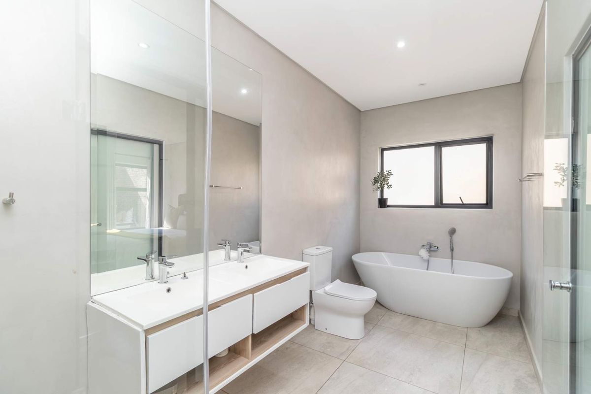 Modern bathroom featuring a double vanity, a sleek freestanding bathtub, large wall mirror, and neutral tiled finishes with contemporary fixtures.