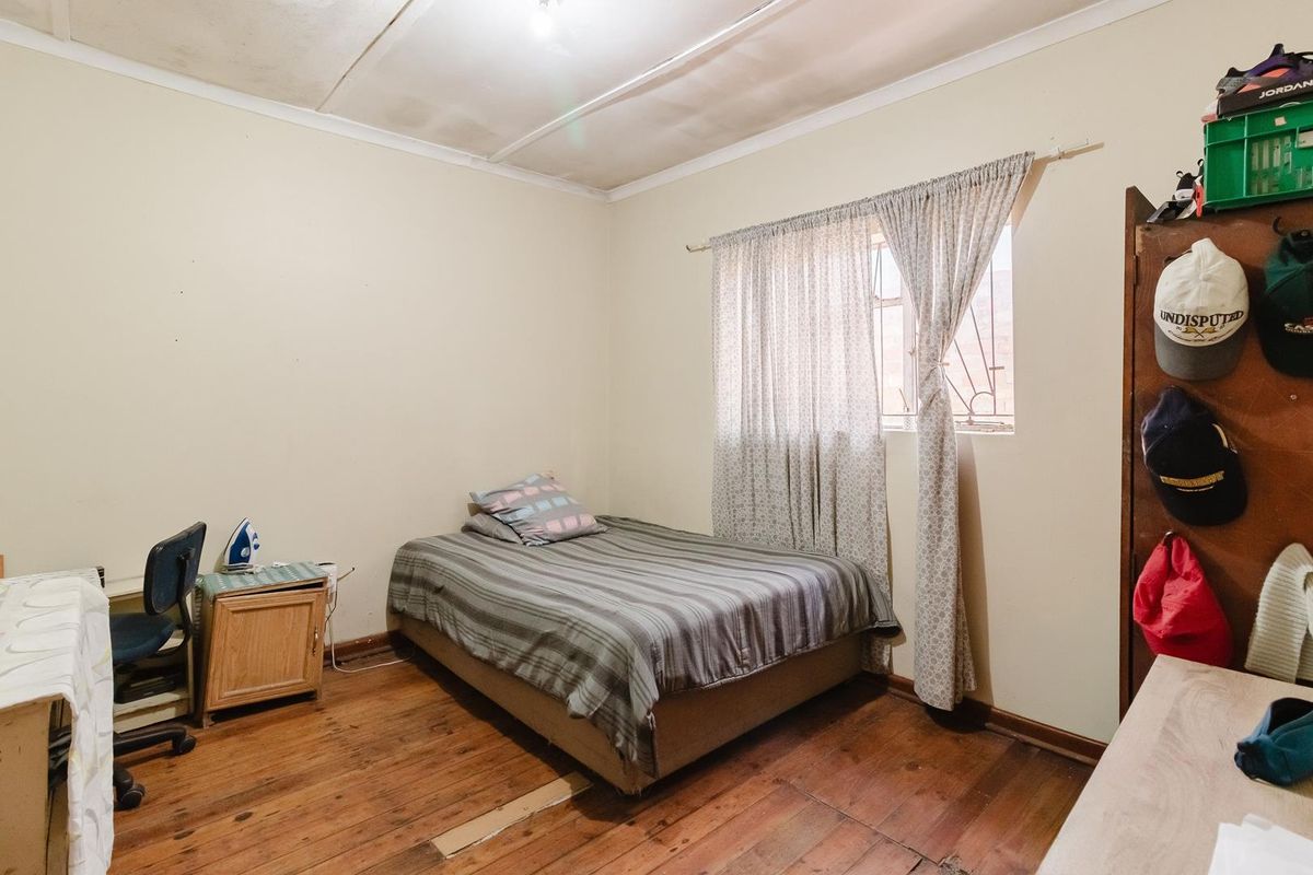 A bedroom featuring original timber flooring, a window with security bars, and a simple ceiling finish.