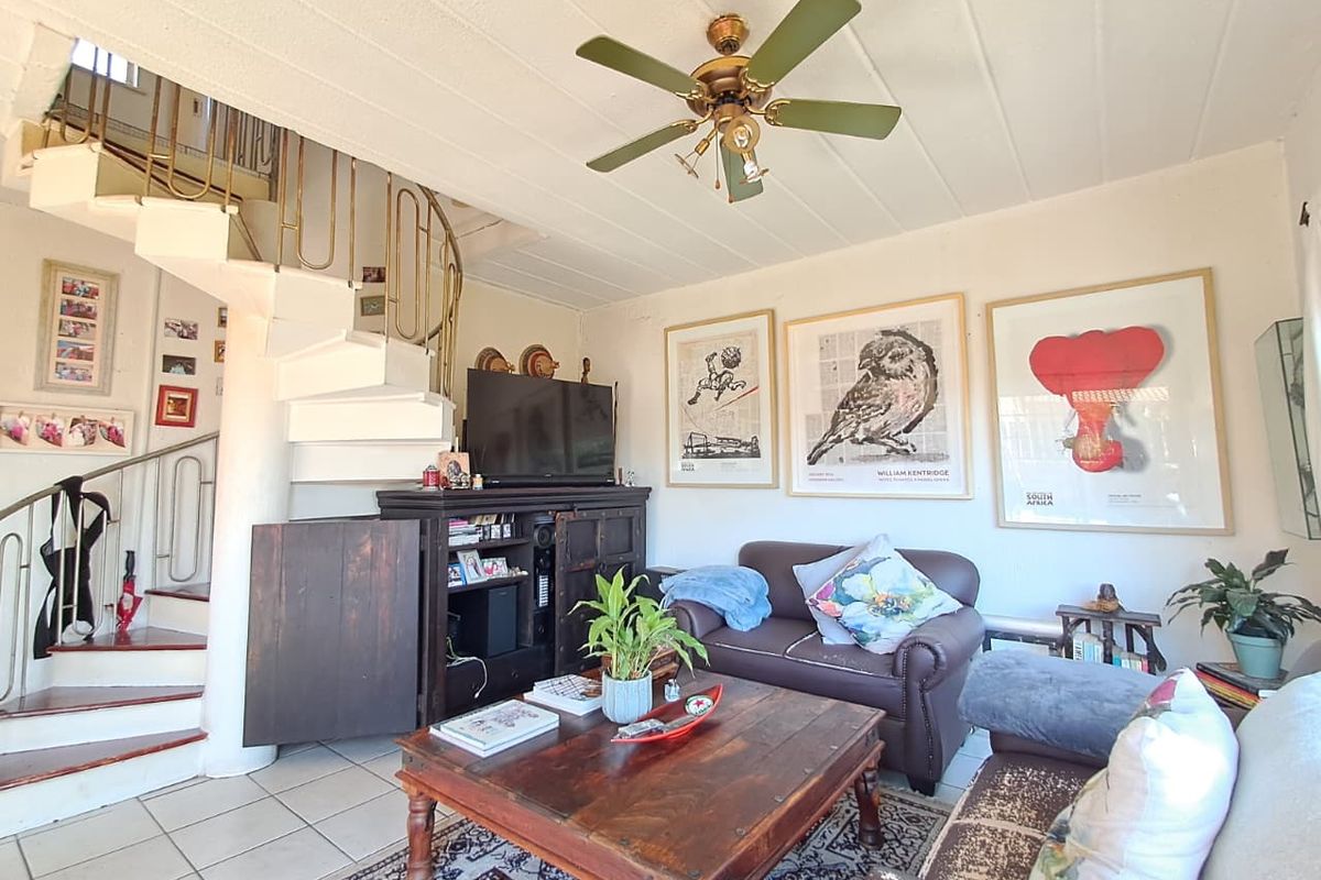 Living room featuring a spiral staircase, tiled flooring, and a ceiling fan, offering a functional layout with potential for modern updates.