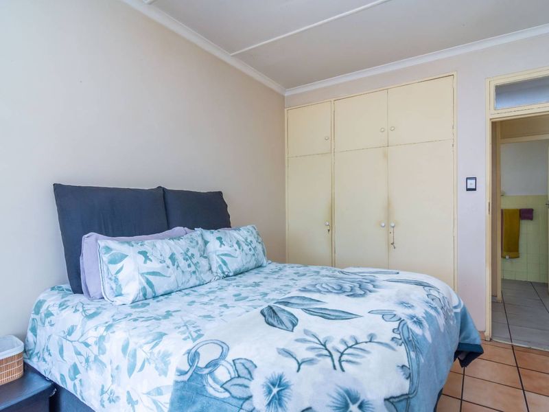 A bedroom featuring built-in cupboards, tiled flooring, and coved ceilings, with an adjacent view into a tiled bathroom area.