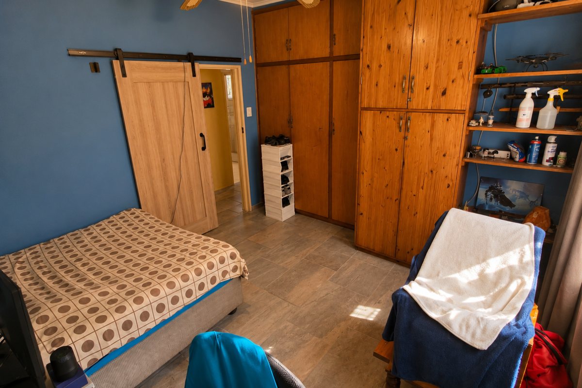 A bedroom featuring built-in wooden cabinetry, tiled flooring, a ceiling fan, and a sliding barn-style door leading to an adjacent room.