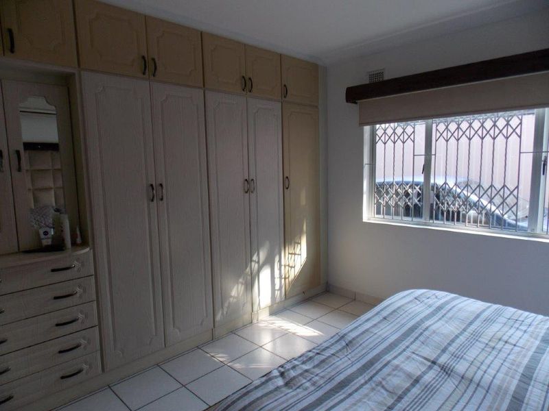 A bedroom featuring extensive built-in cabinetry, tiled flooring, and a window fitted with a security gate.