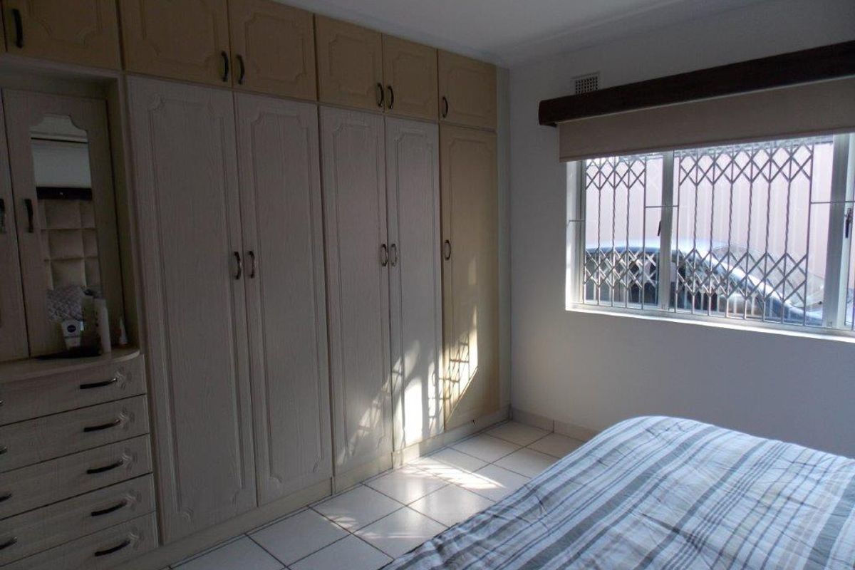 A bedroom featuring extensive built-in cabinetry, tiled flooring, and a window fitted with a security gate.