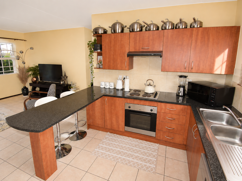 Open-plan kitchen featuring wood-finish cabinetry, granite countertops, integrated appliances, and a breakfast bar, seamlessly flowing into the adjacent living area.