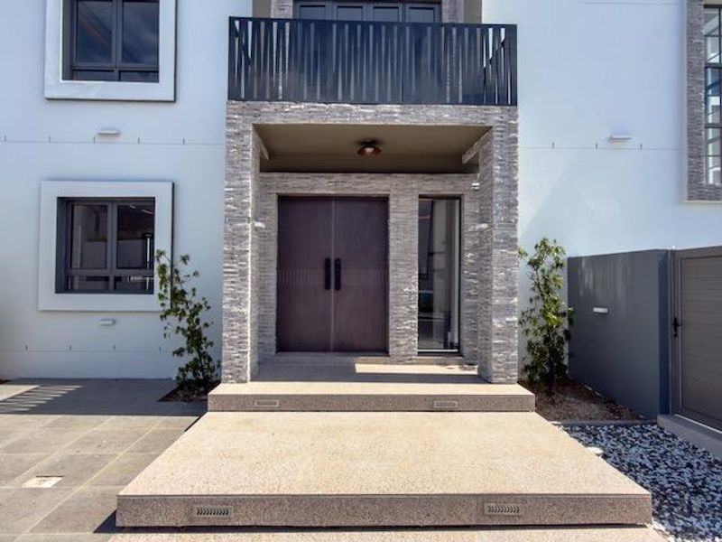 Modern front entrance featuring stone-clad pillars, double doors, a balcony with metal railing, and integrated step lighting.
