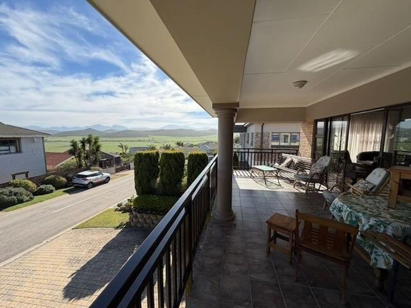 A spacious covered balcony featuring tiled flooring, a metal balustrade, and expansive views of the surrounding landscape and neighborhood.