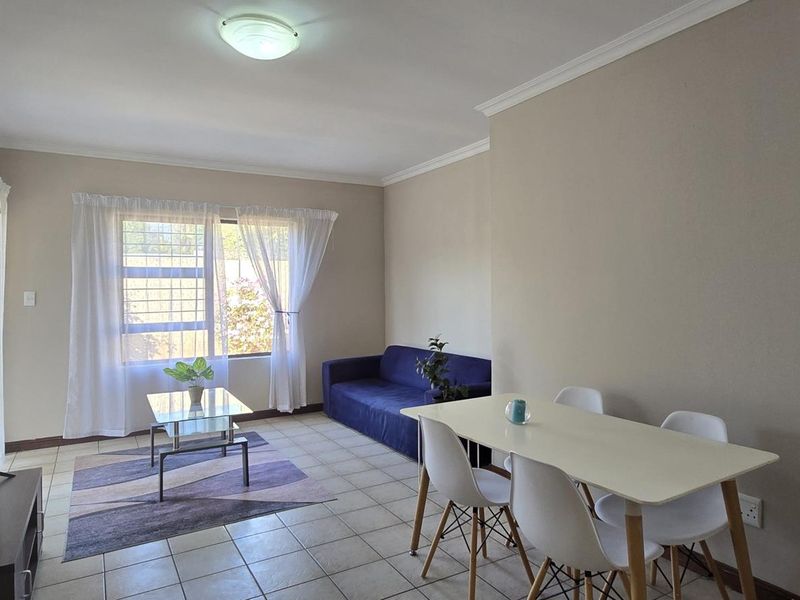 An open-plan living and dining area featuring neutral wall tones, tiled flooring, and a window fitted with security bars.