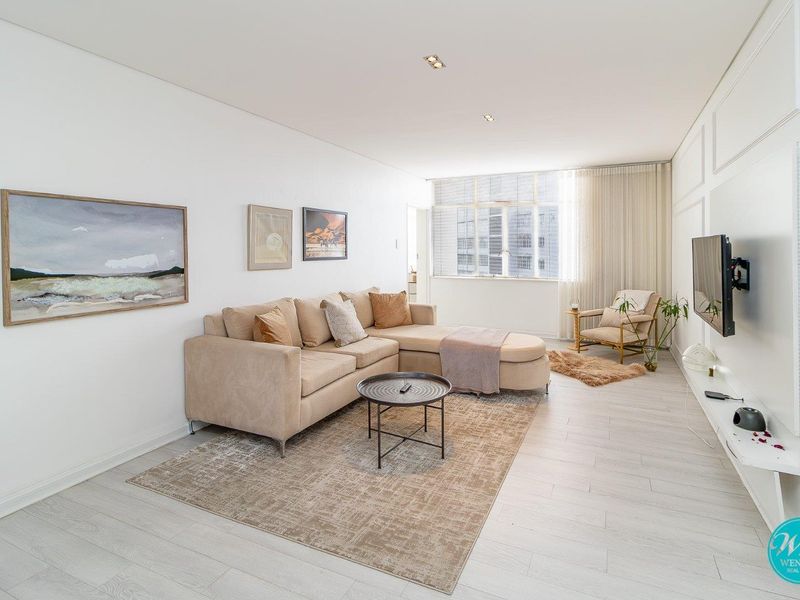 A bright and modern living room featuring light-toned laminate flooring, recessed downlighting, and decorative wall paneling, offering a clean and contemporary aesthetic.