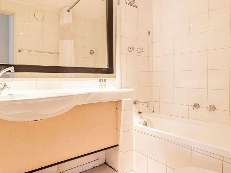 A functional bathroom featuring a wall-mounted basin, built-in bathtub, and tiled walls, offering a clean but dated aesthetic ready for modernization.