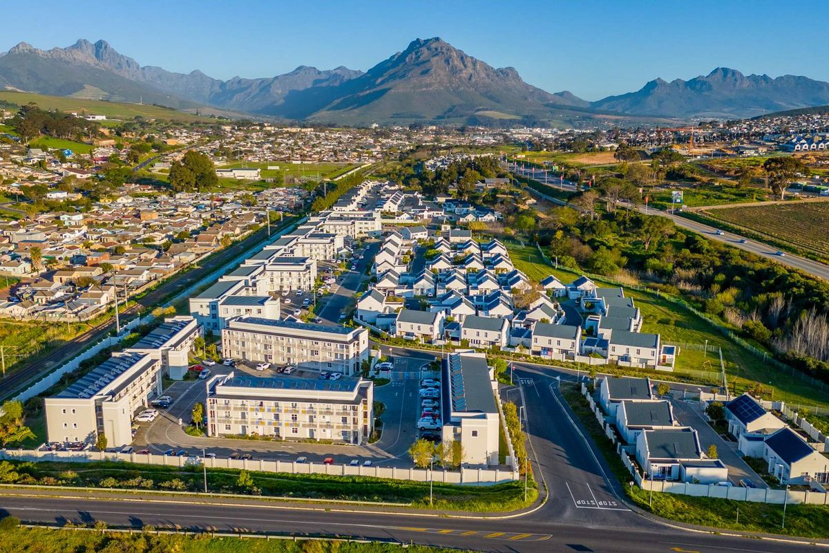 Aerial view of a modern residential apartment complex and housing estate, featuring paved access roads, perimeter security, and mountain views.