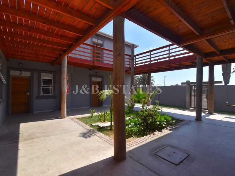 A central courtyard area featuring a covered wooden pergola, concrete flooring, and a raised wooden walkway connecting the building units.