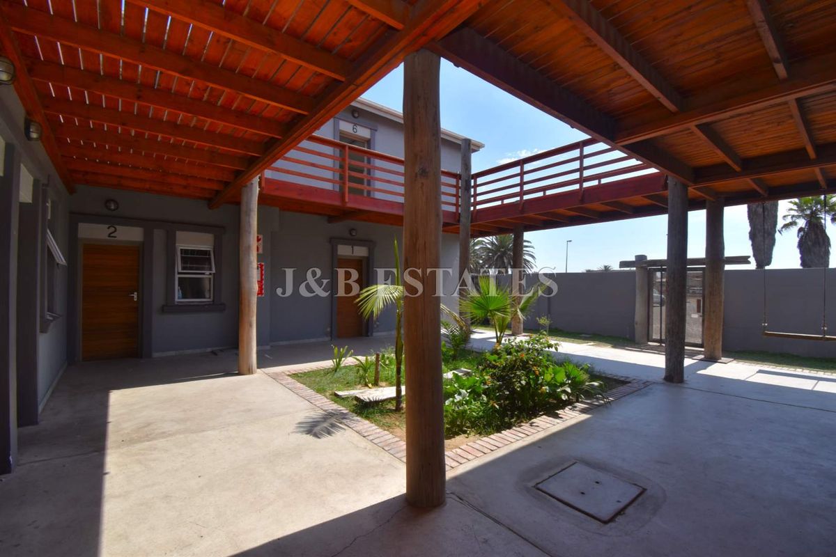 A central courtyard area featuring a covered wooden pergola, concrete flooring, and a raised wooden walkway connecting the building units.