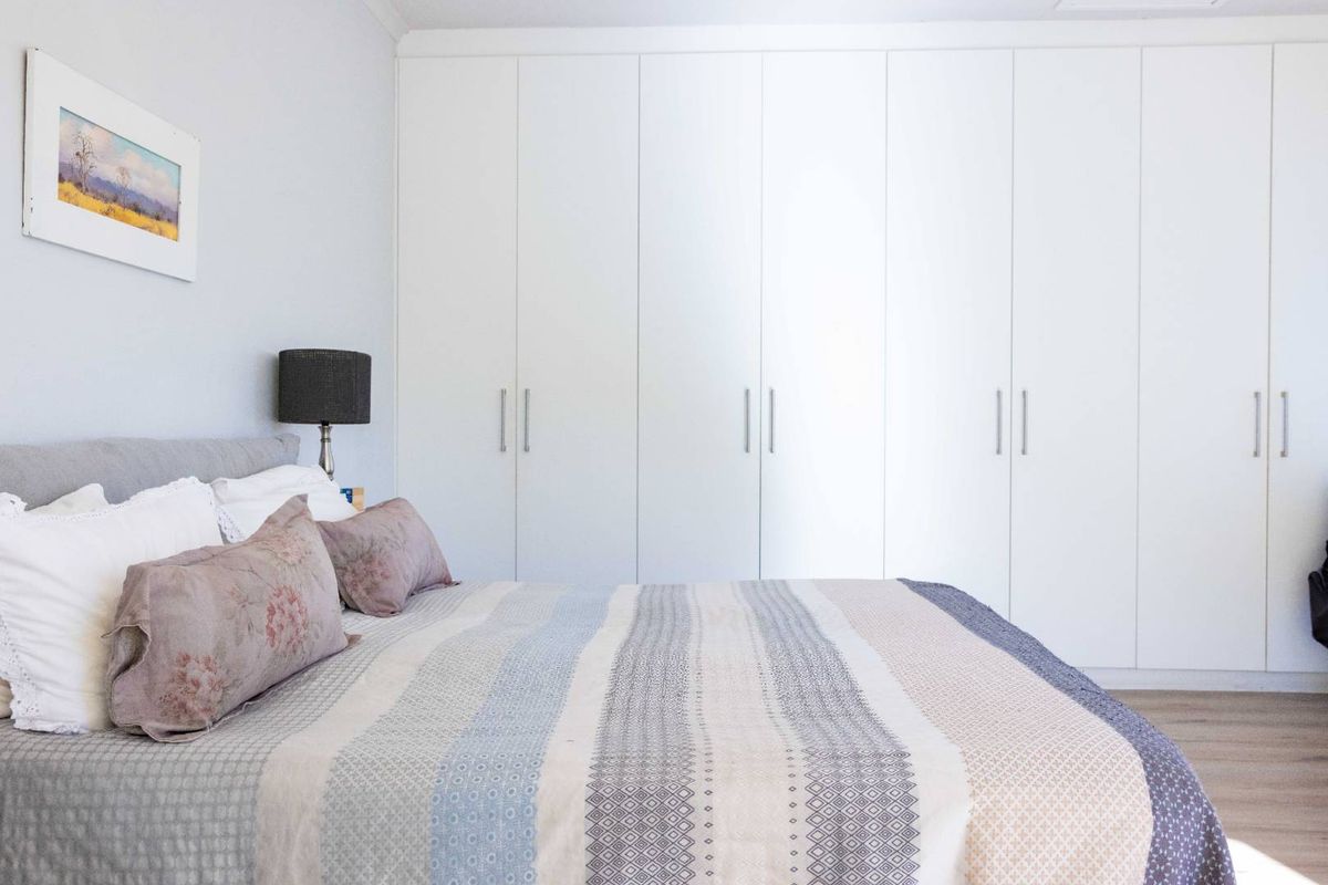 A well-maintained bedroom featuring extensive floor-to-ceiling built-in wardrobes with clean white finishes and modern hardware.